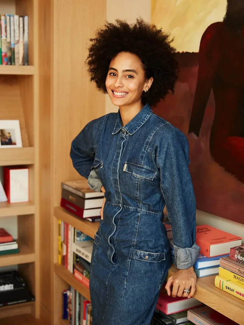 Woman in a denim dress standing beside bookshelves.