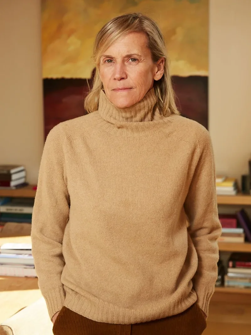 Woman in a tan sweater standing in a room with bookshelves.